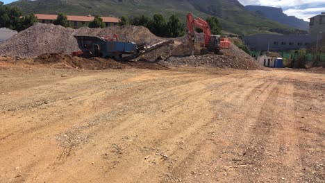 wide shot of hitachi zaxis excavators working on a construction site in cape town, south africa. sunny blue sky afternoon and dusty sand with table mountain in the background.