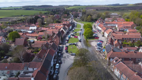 Drohne-Aus-Der-Luft,-Die-An-Einem-Sonnigen-Und-Bewölkten-Tag-In-North-Norfolk,-Großbritannien,-Die-Hauptstraße-Des-Schönen-Alten-Dorfes-Burnham-Market-In-Richtung-St.-Mary&#39;s-Church-Fliegt