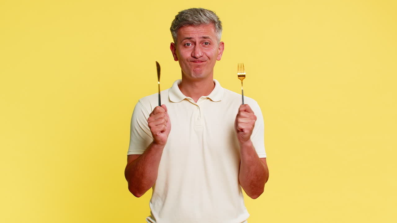 Man holding knife and fork looking at camera with hungry expression waiting for tasty delicious food