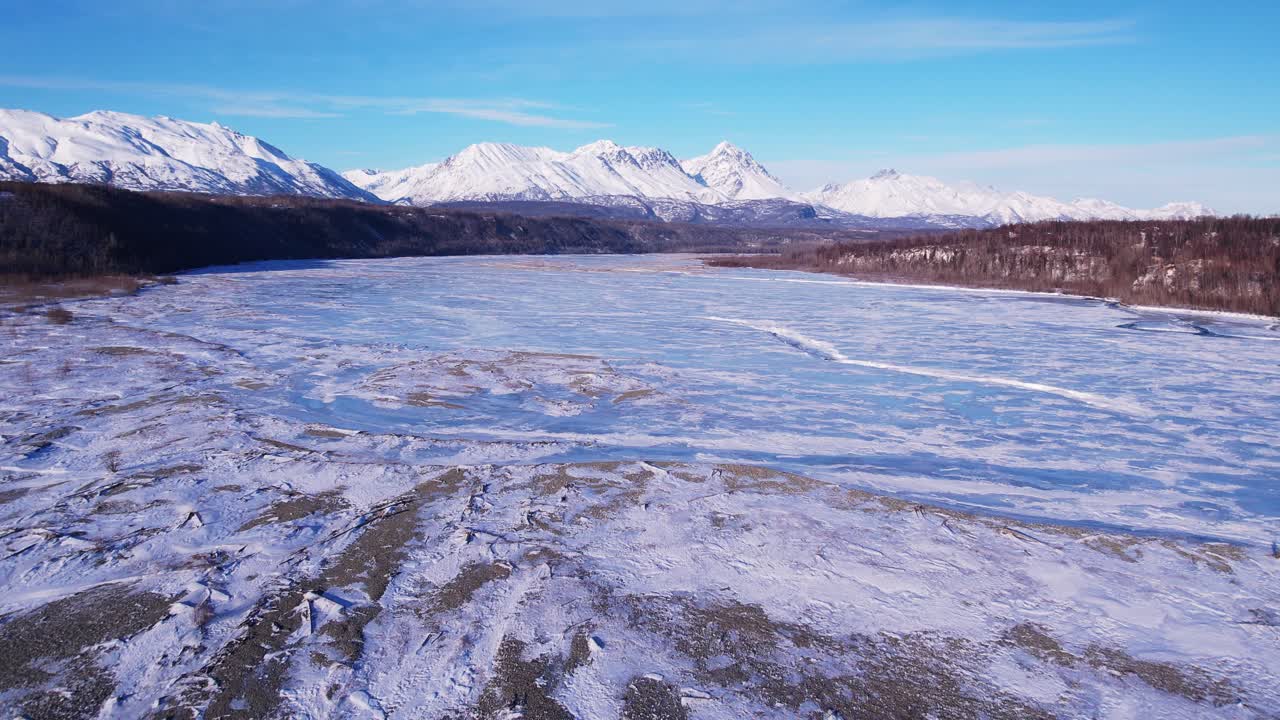 Lavtflyvende drone over delvist frossen Matanuska-flod nær Palmer, AK. Blottede grusbanker ogismønstre fylder forgrunden, mens sneklædte tinder og trægrænsen indrammer den fjerne horisont. DJI Air 2S 4