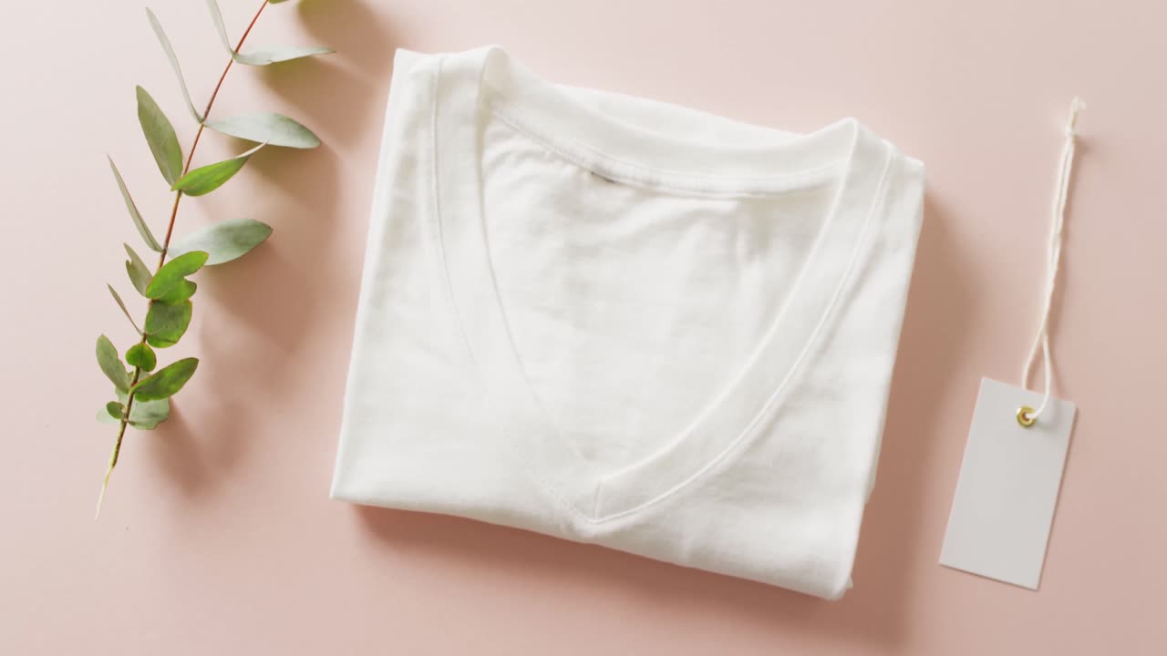 핑크색 배경에 태그를 붙인  ⁇ 색 접힌 티셔츠의 클로즈업 비디오