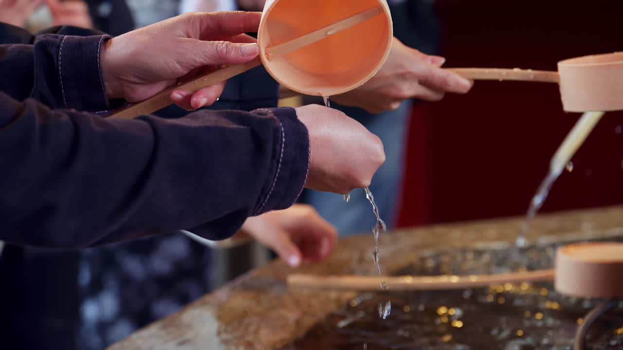 Close up of people performing the purification ritual at a water fountain at the Senso-ji temple in daylight in Tokyo, Japan