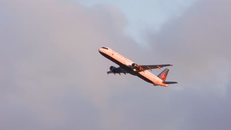 airplane banking on takeoff at sunset with a partially cloudy sky