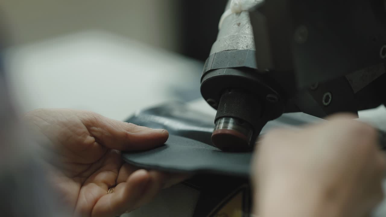 Closeup of worker guiding leather under industrial embossing machine creating textured surface during footwear manufacturing