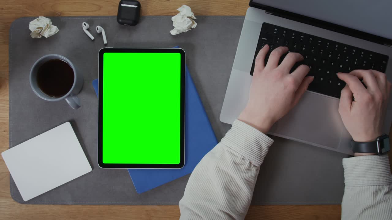 una tableta con una pantalla verde se encuentra en el escritorio siguiente escribiendo en el portátil hombre