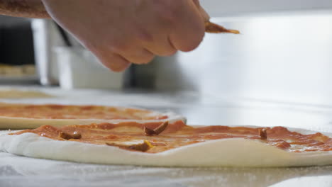 primer plano de un chef irreconocible apretando una manga pastelera y agregando salsa picante calabresa 'nduja en la masa cruda de pizza en el restaurante