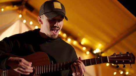 man plays the guitar and sings songs in a tent with light bulbs