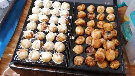 Brutzelnde-Japanische-Takoyaki-Tintenfischbällchen,-Köstliche-Goldbraune-Streetfood-Snacks,-Die-Auf-Einer-Heißen-Platte-Kochen