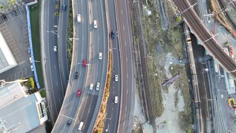 top down shot from above brisbane city's mayne railway yard, as a train passes through the shot, busy car traffic on road leading to icb inner city bypass