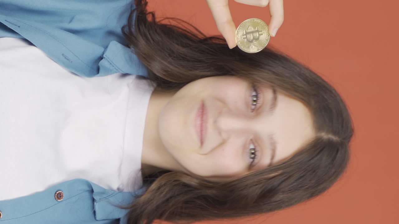 video vertical de una mujer joven sosteniendo bitcoin y mostrándolo.