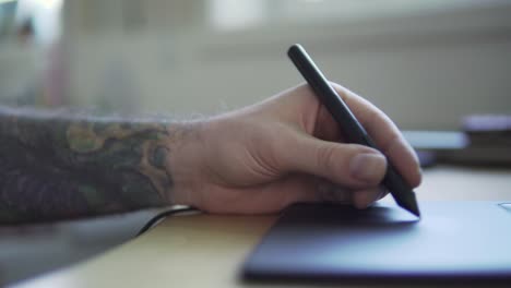 una persona con un brazo tatuado está dibujando algo en una tableta gráfica