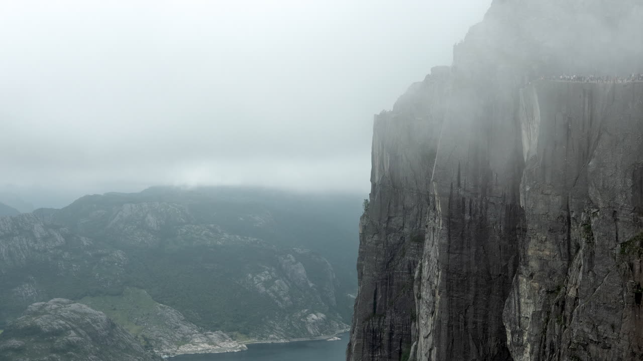 impresionante lapso de tiempo de la roca del púlpito, preikestolen en noruega, una gran cantidad de turistas se reúnen en el acantilado, día nublado con niebla, turismo de masas en mal tiempo