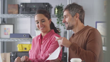 Male-And-Female-Designers-In-Studio-Making-Video-Call-And-Showing-Designs-At-Desk-On-Laptop