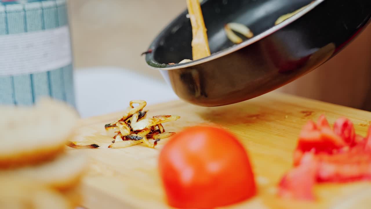 Hot fried onions placed from pan to wooden board with fresh tomato, slow motion