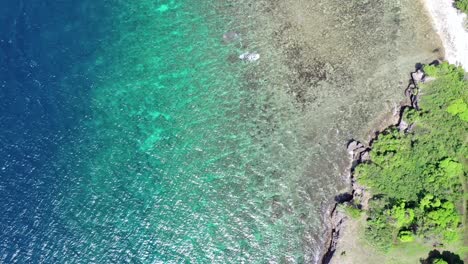 Aerial-bird's-eye-view-above-turquoise-tropical-water-with-barrier-reef-near-a-coastline-with-green-trees-around,-travel-concept