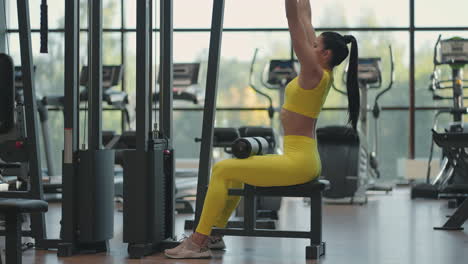 hispanic woman sitting on a simulator in the gym pulls a metal rope with the weight pumps up the muscles of the back. brunette woman pulls on simulator. performing exercise for back muscles simulator