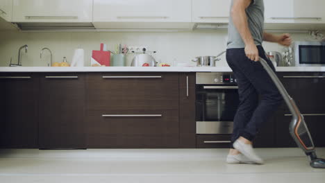 Happy-man-cleaning-floor-with-vacuum-cleaner-at-kitchen-in-slow-motion.