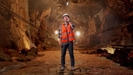 full body of asian male engineer with safety helmet yelling with hand over mouth while standing in underground mine tunnel