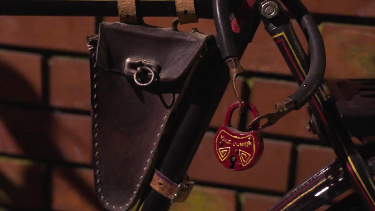 A close-up of a vintage bicycle’s frame bag and red padlock, mounted on the frame at night
