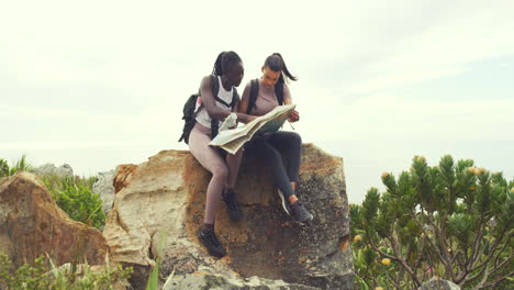 two women hiking looking at map sitting on a rock