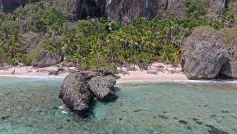 Narrow-strip-of-beach-with-huge-dropped-rocks-and-people-swimming,-playing