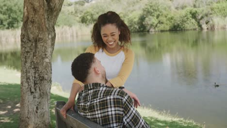 feliz pareja afroamericana sentada en un banco en el lago en el bosque, cámara lenta