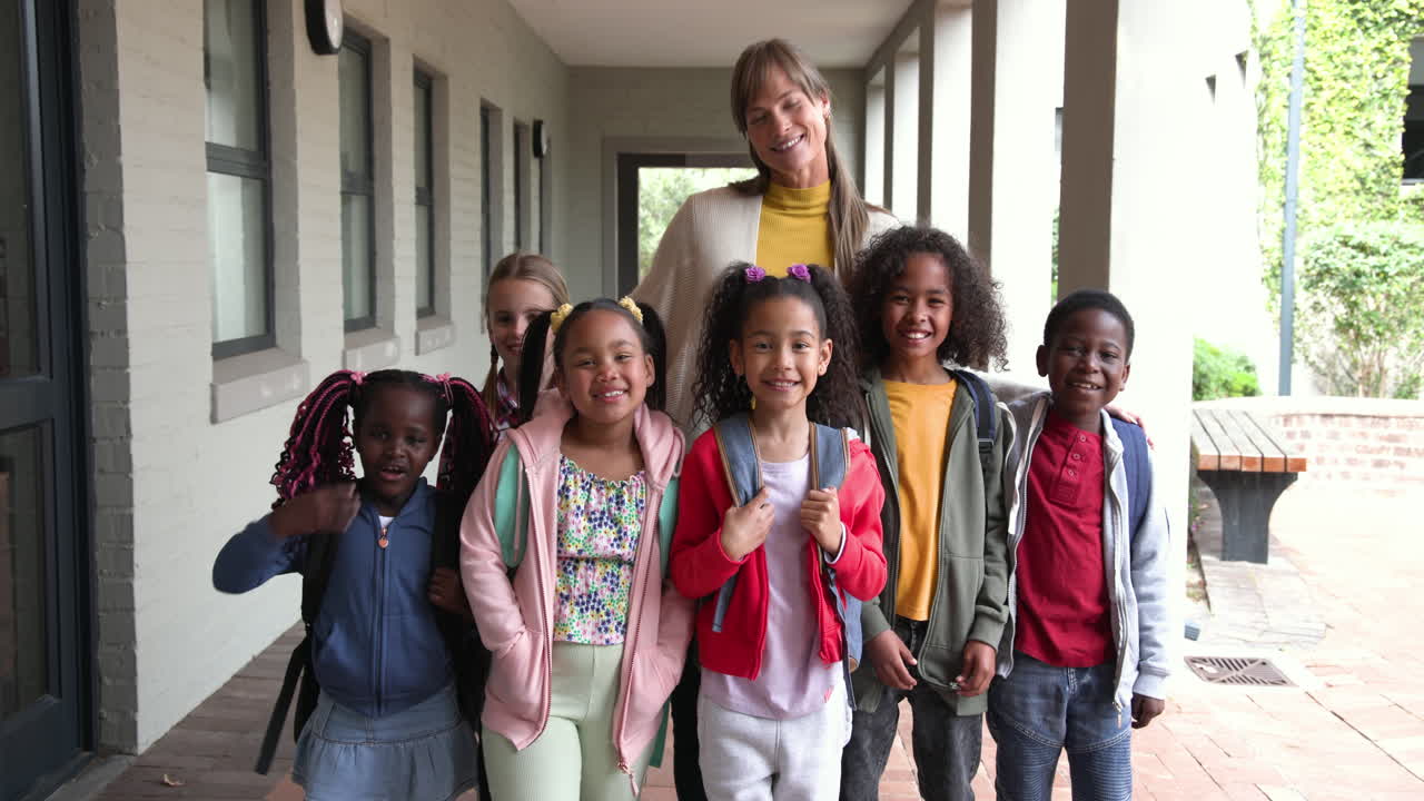 Smiling teacher with diverse group of children standing together at school entrance