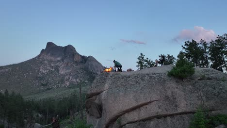 man tends campfire atop boulder with sheeprock views, camping in san isabel