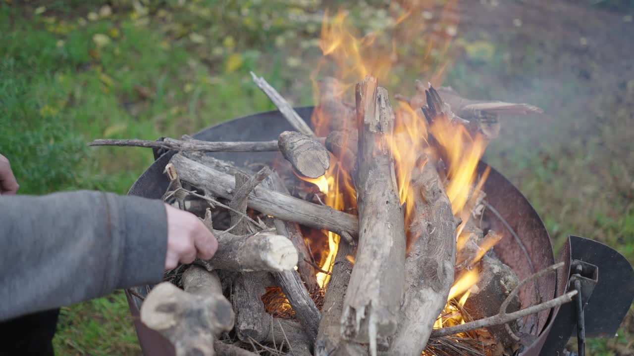 Person legger ved på et bål i en bålpanne av metall
