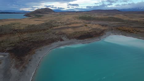 vibrant blue lake tekapo with hilly peninsula on cloudy day on south island of new zealand. aerial shot