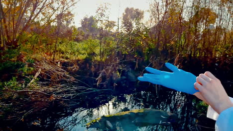 a young woman scientist at a creek, in a lab coat, putting blue latex-nitrile gloves on her right hand