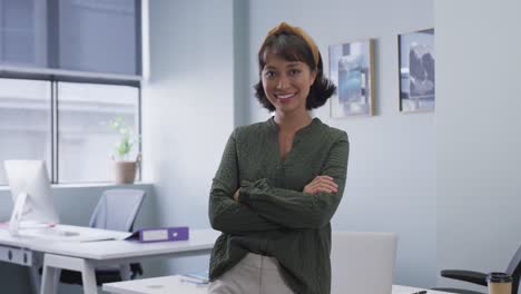 Portrait-of-biracial-businesswoman-smiling-with-arms-crossed-alone-at-office