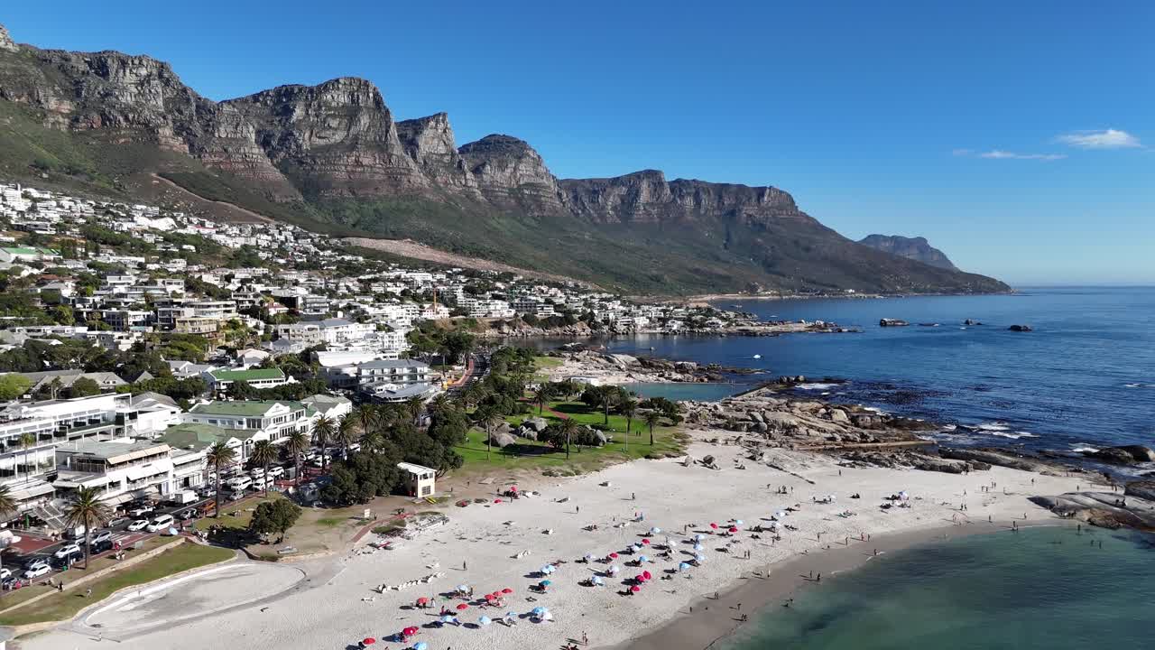 Cinematic drone shot of Lion’s Head mountain and Camps Bay beach in Cape Town , South Africa Atlantic coastline aerial perspective showcasing ocean waves, sandy beach, tourists sunbathing