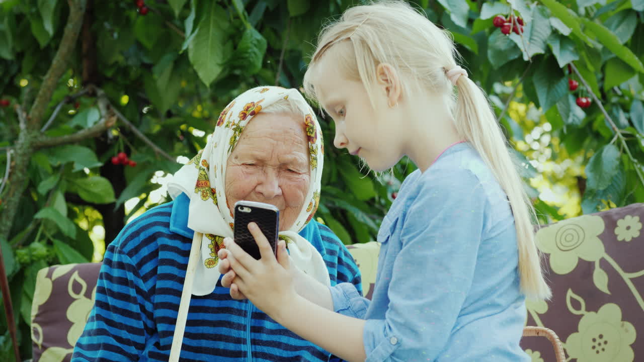 그 소녀는 세대 개념 4k 비디오의 스마트폰 친교에 할머니 사진을 보여줍니다