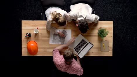 three workers discuss plan of building and watch laptop, teamwork concept, office concept, communication concept