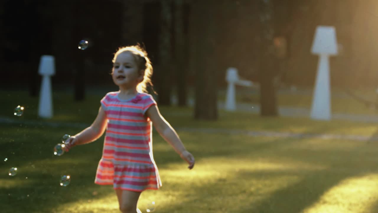 Little beautiful girl catches bubbles at sunset in slow motion
