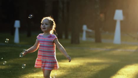 little beautiful girl catches bubbles at sunset in slow motion