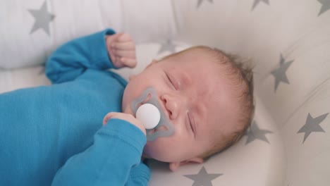 cute little baby with dummy cries sleeping in cocoon in crib