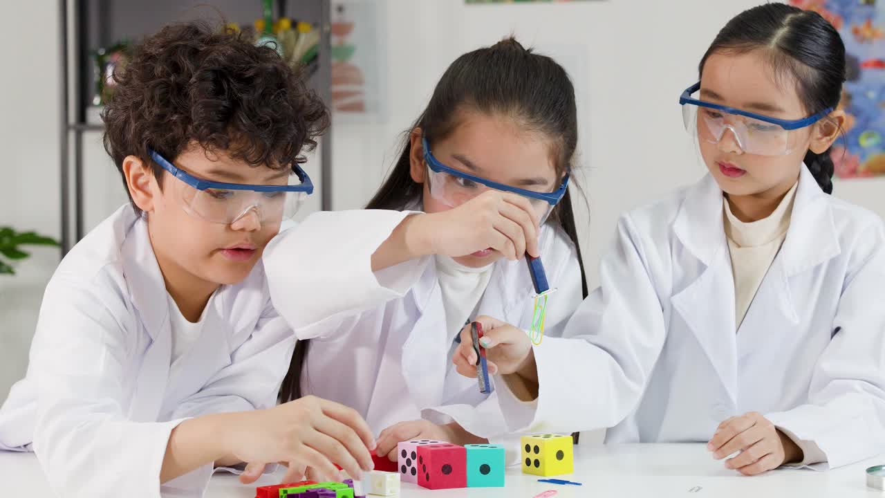 Tiga siswa SD mengenakan kacamata pelindung dan jas lab saat menjelajahi magnetisme dengan balok warna-warni