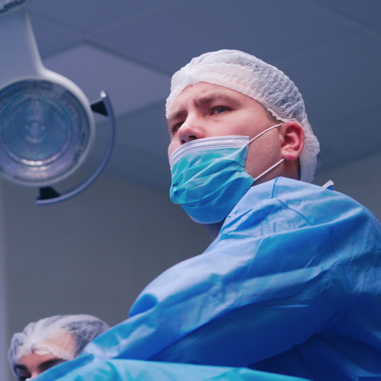 Portrait of male surgeon. Doctor in mask and protective uniform looking ahead seriously. Surgeon and a nurse during the operation in clinic.