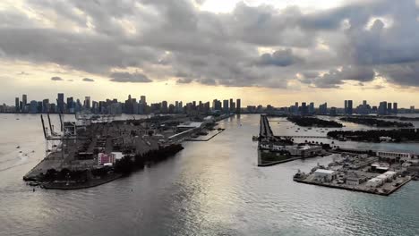 Drone-footage-of-a-cargo-vessel-entering-the-Port-of-Miami-from-the-Atlantic-Ocean,-showcasing-the-Miami-skyline-behind-it