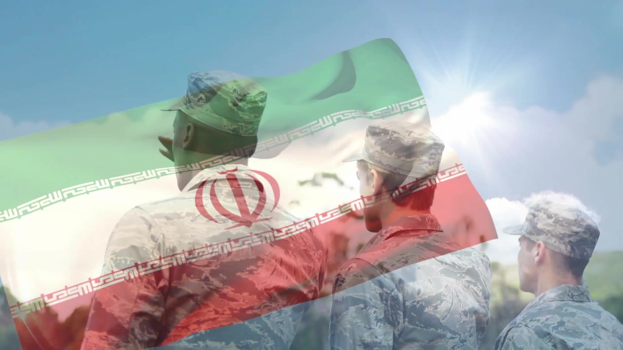 Hembusan angin menyebabkan bendera Iran berkibar di antara tentara yang berdiri dalam formasi pertahanan di lapangan.