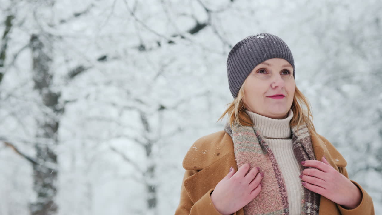 una mujer satisfecha camina en un parque de invierno y se regocija con el hermoso clima nevado