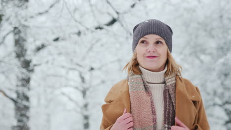 una mujer satisfecha camina en un parque de invierno y se regocija con el hermoso clima nevado