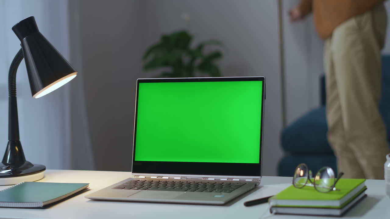 portátil con pantalla de llave croma en la mesa de trabajo en la sala de estar hombre está encendiendo la lámpara de piso y tomando gafas oficina de casa de freelancer