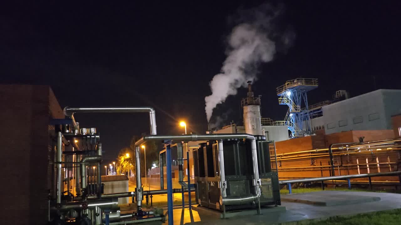 General shot at night in a chemical factory with normal time starry sky and steam chimney releasing steam