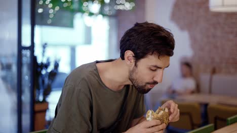 unshaven c man eats meat burger with pleasure, bites burger with his mouth