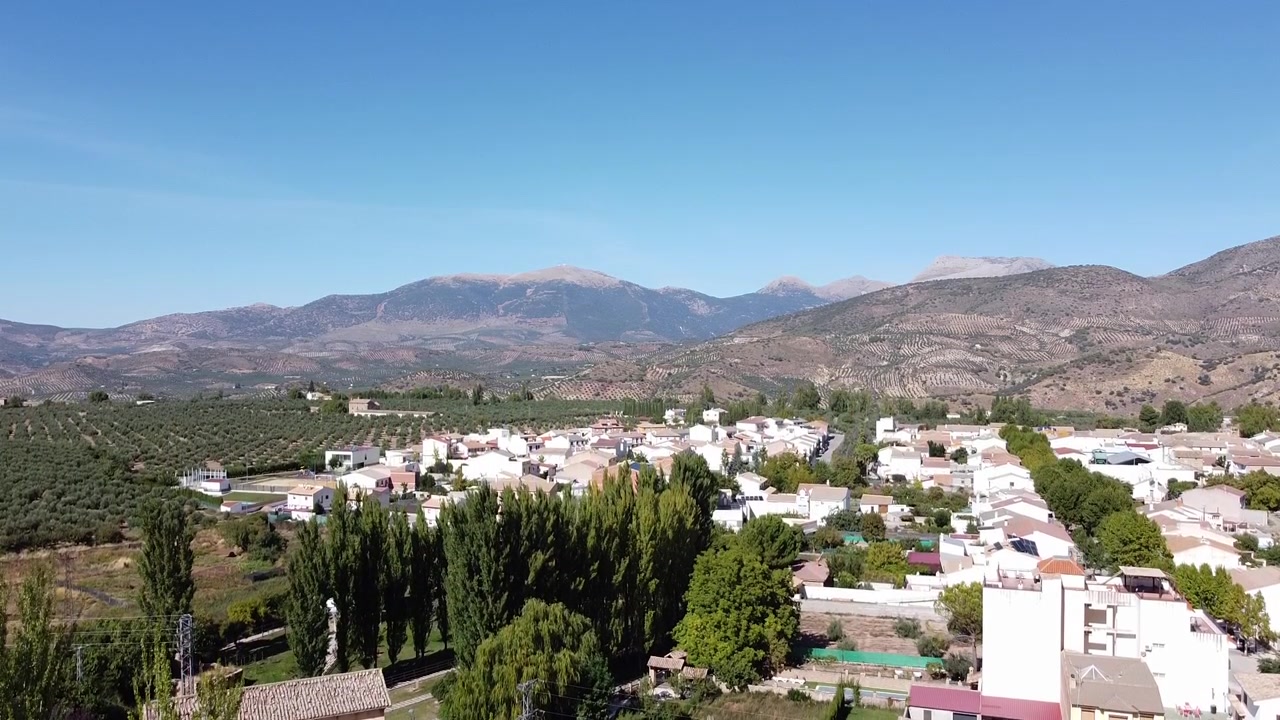Yemyeşil ağaçlarla çevrili, kristal berraklığında doğal bir kaynak, güney İspanya'da geleneksel bir kırsal köyü ve dağlık manzarayı gözler önüne seriyor.