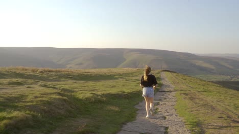 Stabilisierte-Aufnahme-Einer-Jungen-Blonden-Frau,-Die-Auf-Dem-Mam-Tor,-Castleton,-Peak-District,-England,-Den-Weg-Entlang-Joggt