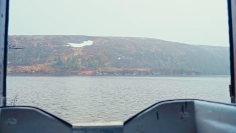 pov from boat on reinsjoen lake in afjord, norway, facing misty hillside on cloudy day. static shot